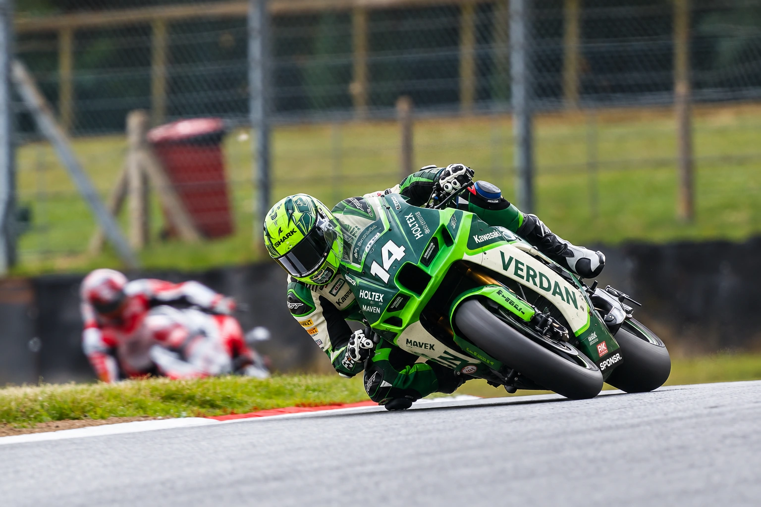 A green Kawasaki superbike at full lean through a corner, another rider behind (SPONSR livery concept).