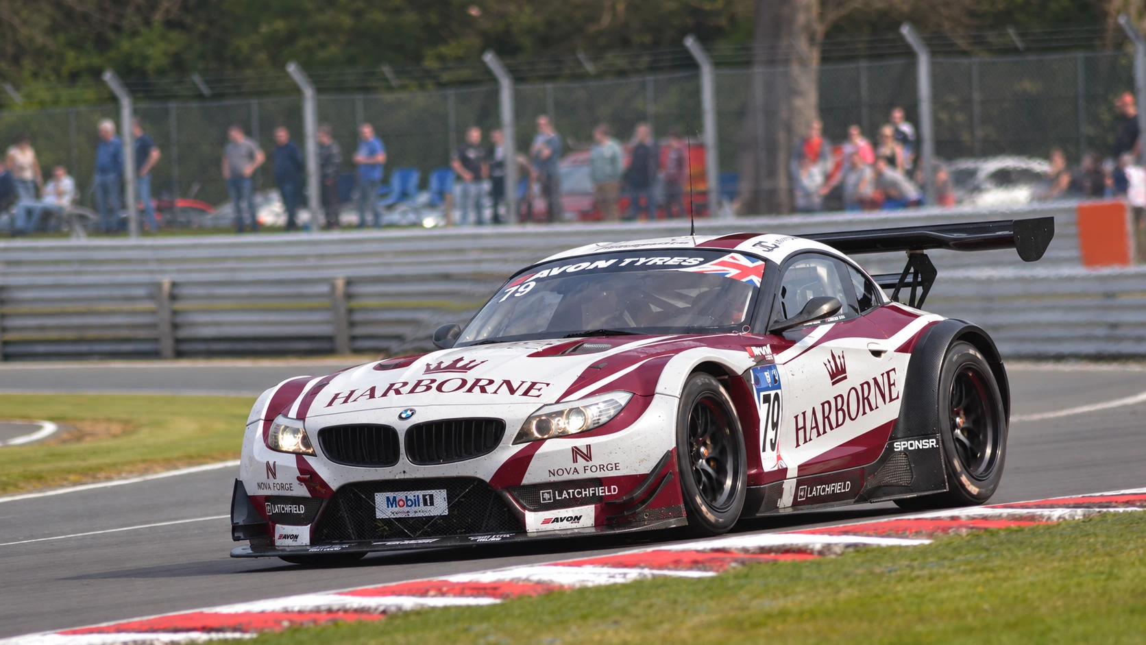 A white and maroon BMW GT car through a corner, spectators lining the fence behind (SPONSR livery concept).